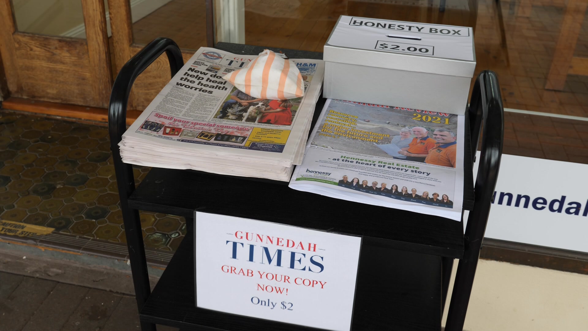 Newspapers on a bench with a box for people to put money in 