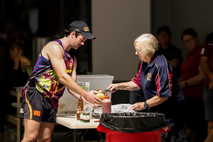 An older woman serves a lamb roll to a young man wearing a singlet and shorts