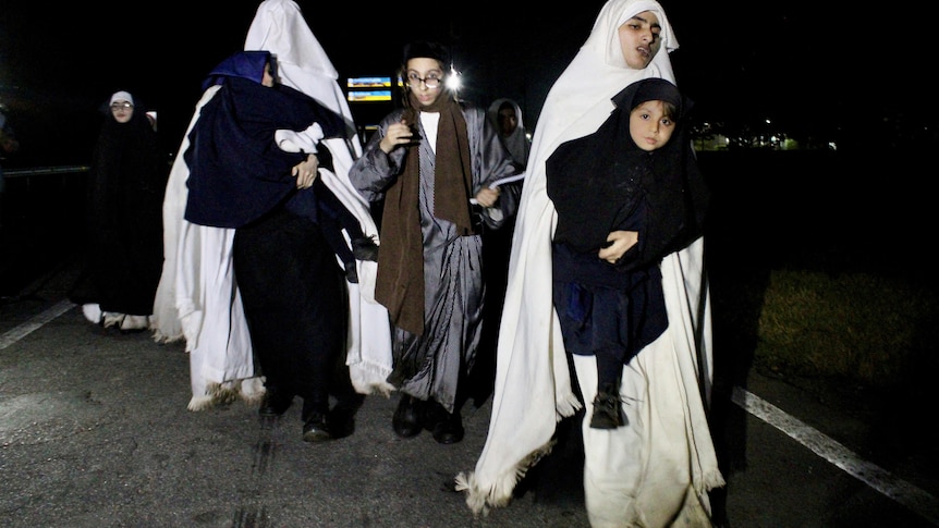 women in full white robes and head covers carry young children in black robes