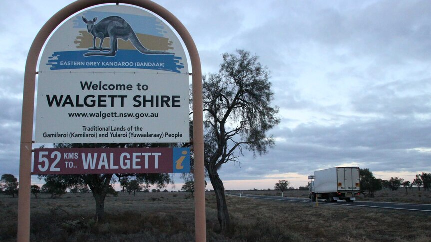 A sign entering visitors to Walgett Shire, with a car and highway off to the right