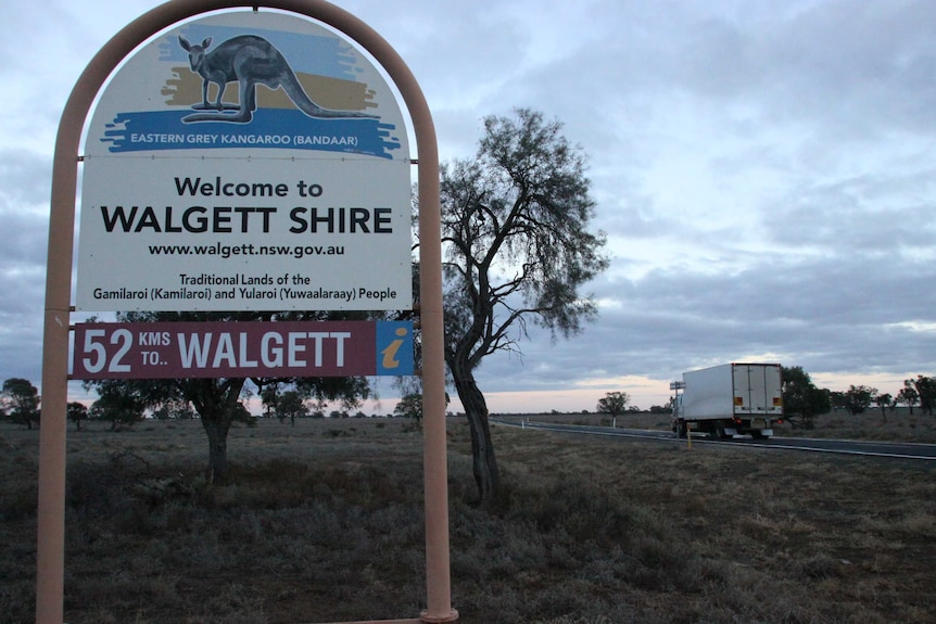 A sign entering visitors to Walgett Shire, with a car and highway off to the right