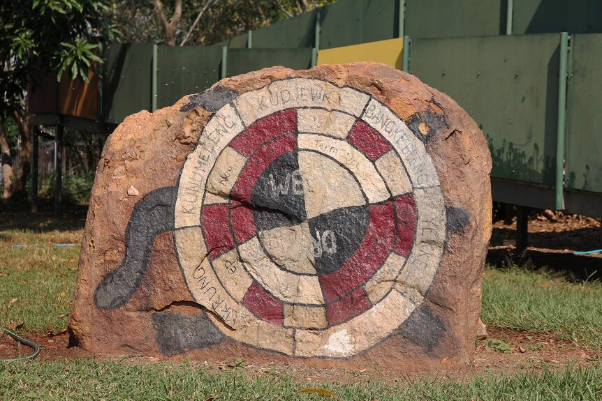A photo of the painted rock depicting the flexible calendar that sits in front of the Gunbalanya school.