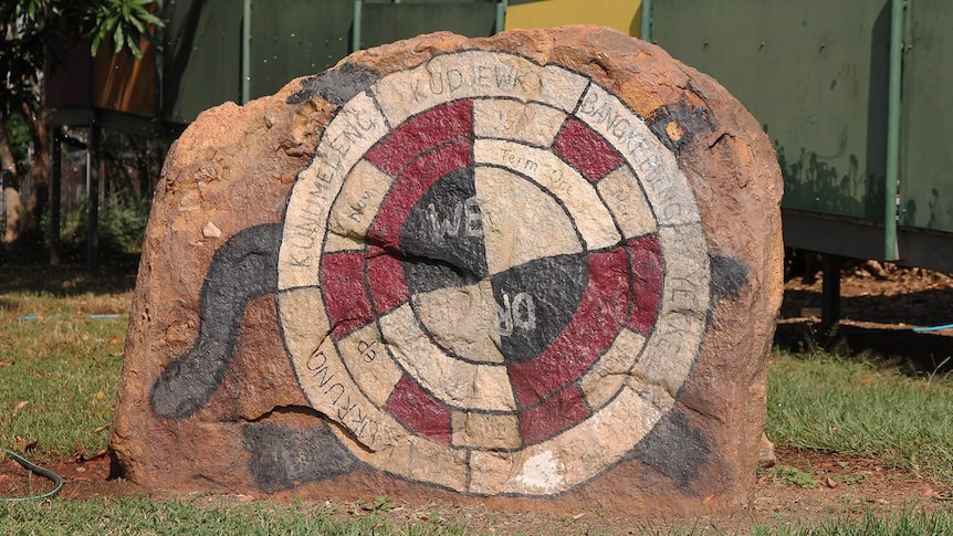 A photo of the painted rock depicting the flexible calendar that sits in front of the Gunbalanya school.