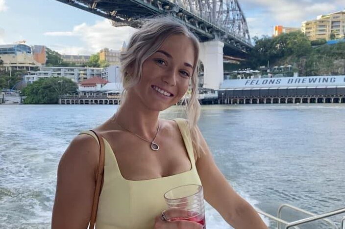 A young lady holding a drink in front of the Story Bridge.