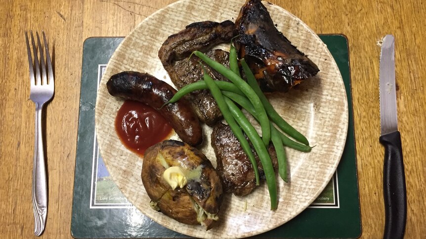 A dinner plate and cutlery with barbecued lamb chops, sausages, potato and green beans.