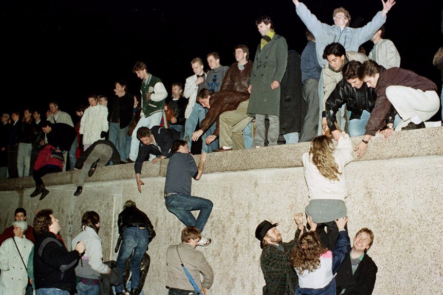 An aged photo of lots of people climbing up and standing on a wall