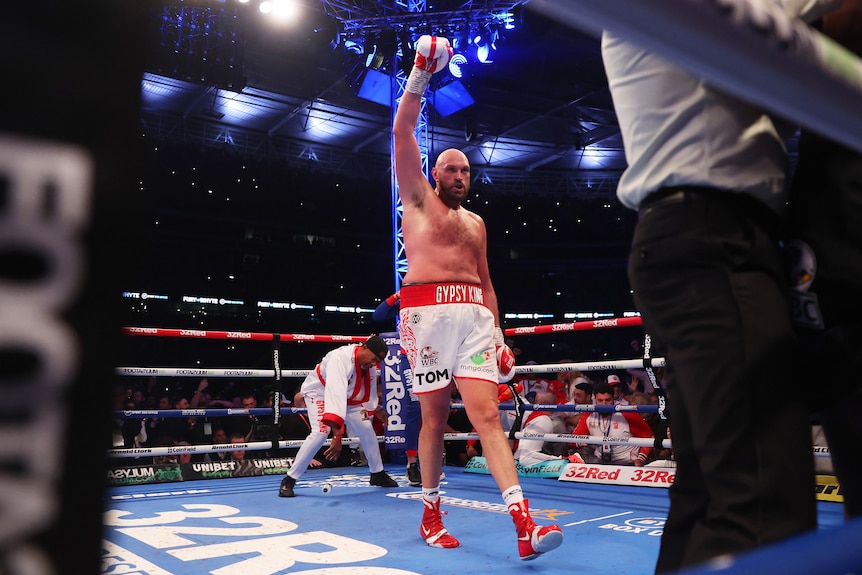 Boxer Tyson Fury walks across the ring with one arm raised in triumph after the end of his fight.