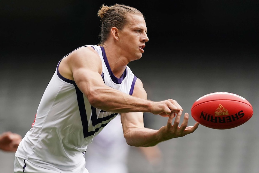 A mid shot of Dockers captain Nat Fyfe handballing a football wearing his white Fremantle jersey.