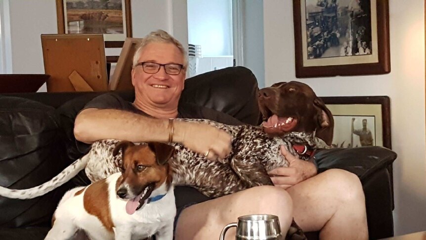 Man sits on a couch and holds two dogs.