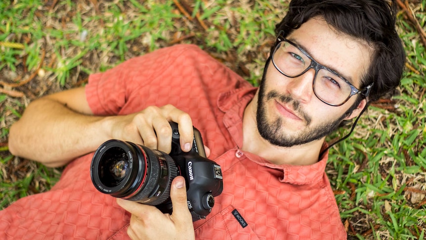 Garrett Eckerson lies back on grass holding a camera.