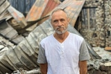 A man stands in front of the shell of a stone-built house that was destroyed by bushfire.