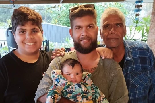 Sam May holds his infant son. Cassius Turvey and his father Sam Turvey stand either side of him.