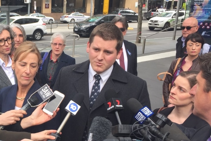 Felix Kostiuk is dressed in a black jacket as he speaks to reporters outside court.