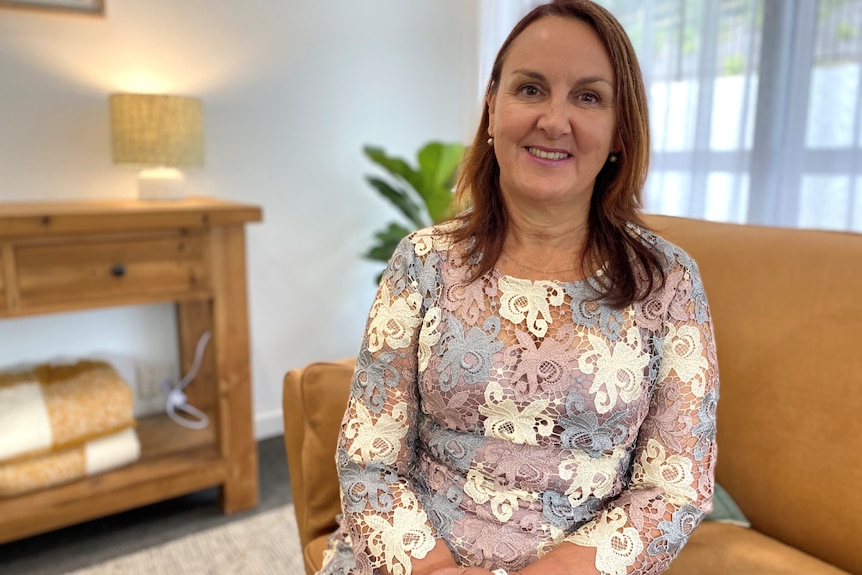 Woman in corporate attire sits in a softly lit lounge room, smiling.