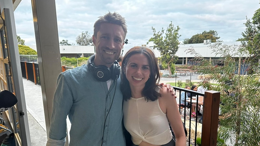 a man wearing headphones smiles with friendly arm around woman