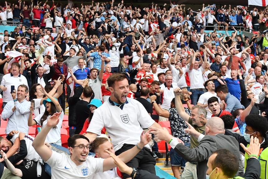 A stand full of England fans celebrate wildly, jumping on chairs and hugging each other