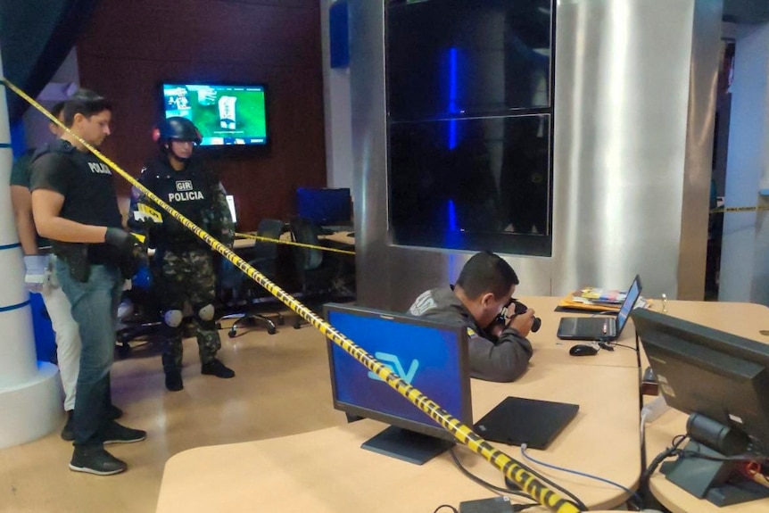 Three police officers look on as another takes photographs of a crime scene