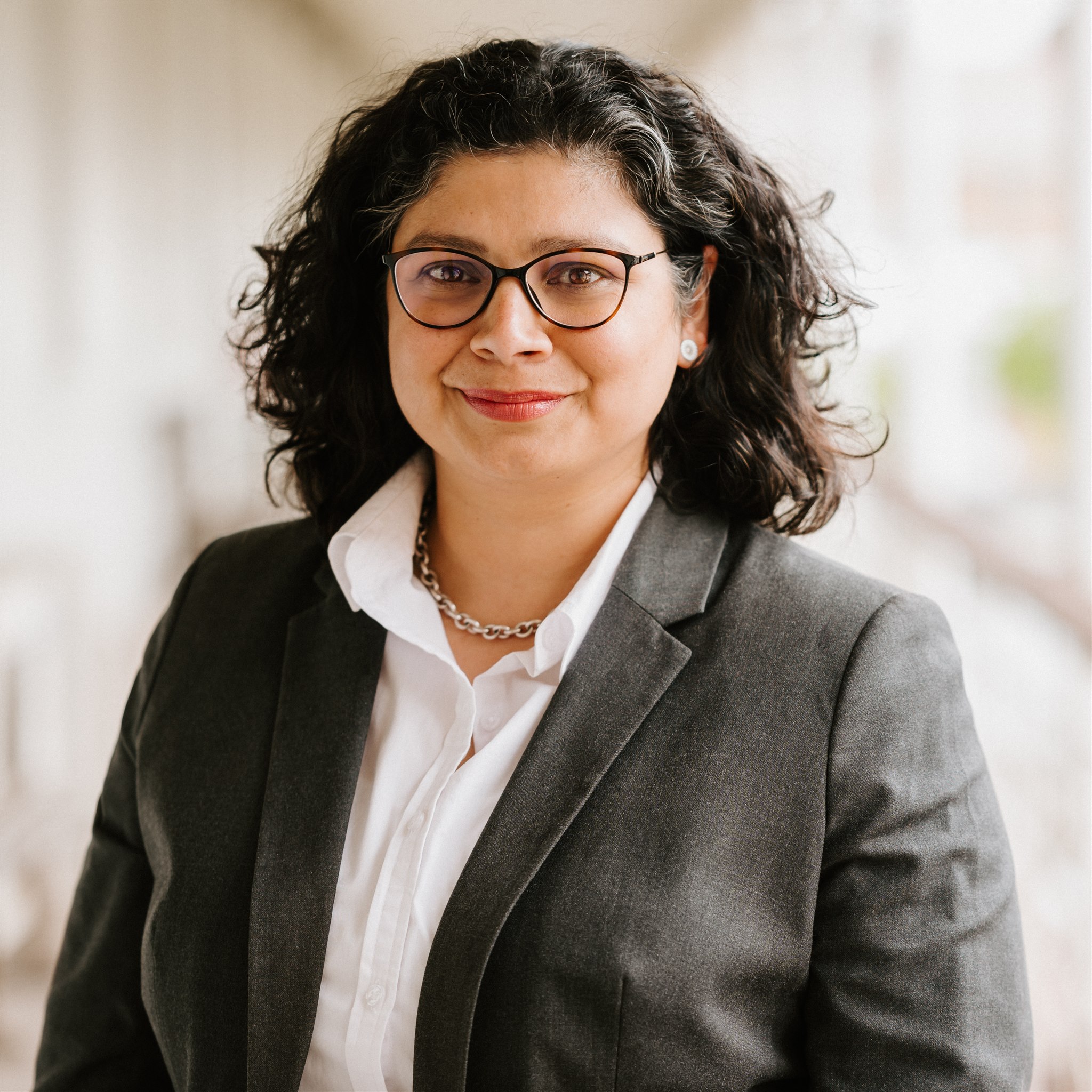 Mujer con gafas, traje gris y pelo rizado en la foto de empresa.