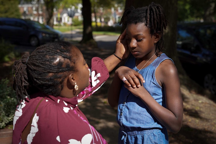 A mum tenderly cups her young daughter's face on a suburban street
