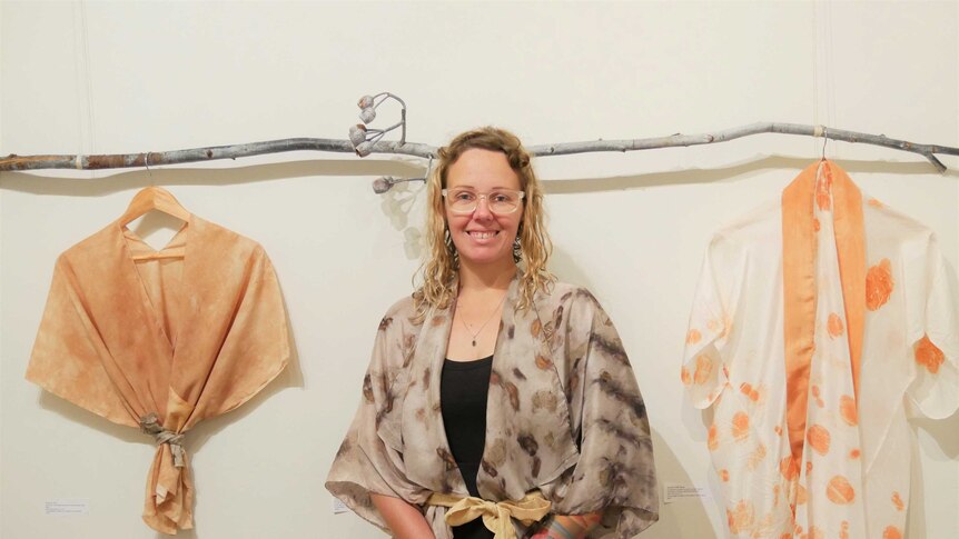 A woman stands in front of some hanging pieces of clothing inside an art gallery.