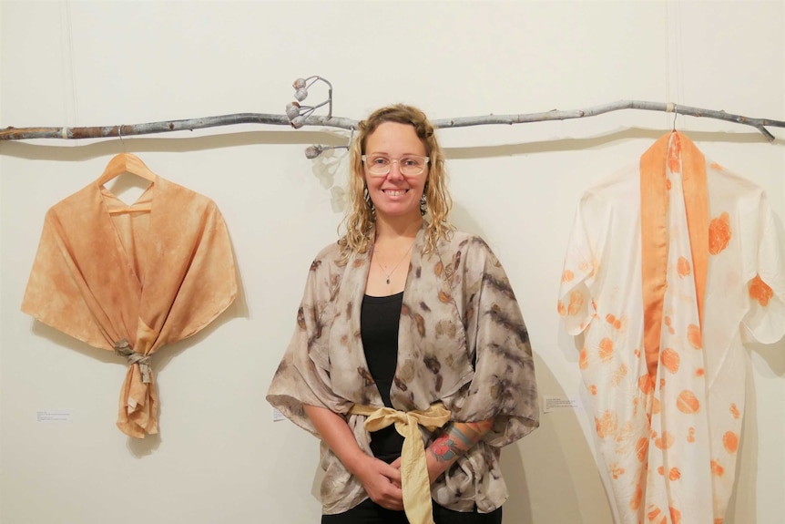 A woman stands in front of some hanging pieces of clothing inside an art gallery.