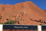 Climbers go up Uluru with a sign below asking people not to.