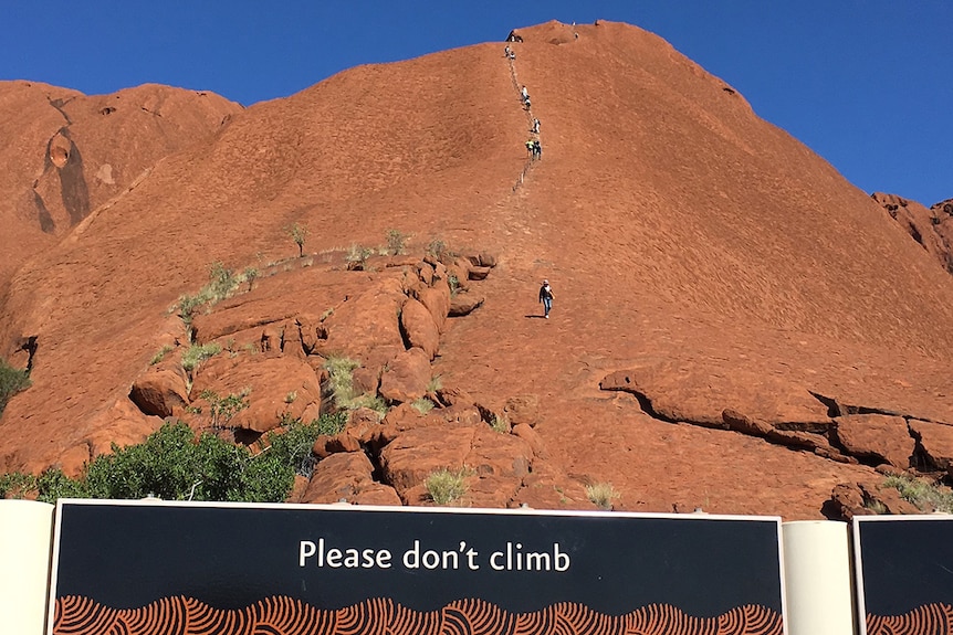 Climbers go up Uluru with a sign below asking people not to.