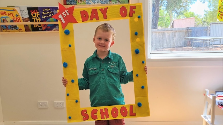 A young boy with a green shirt smiling and holding a yellow rectangular banner