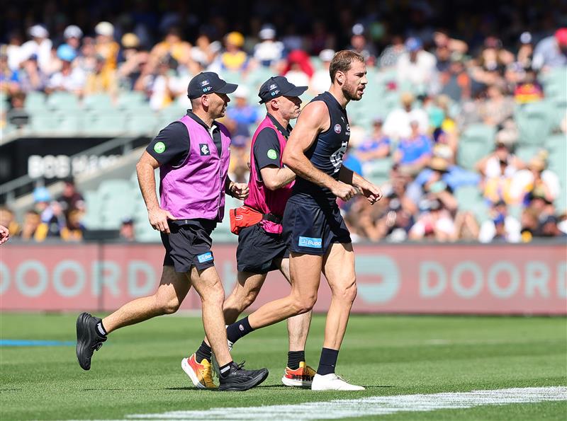 Harry McKay runs off the field while flanked by Carlton medical staff