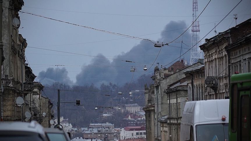 Black smoke is seen in the distance over an urban street