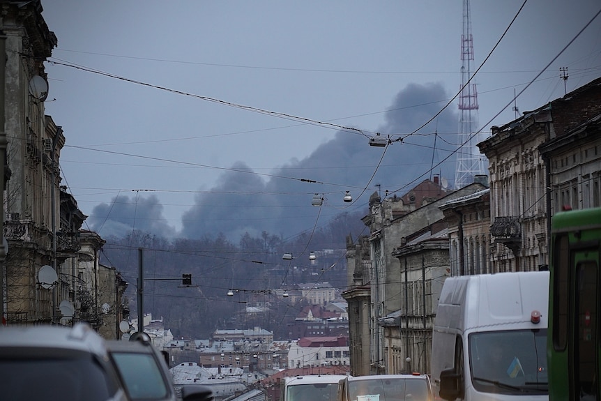 Black smoke is seen in the distance over an urban street