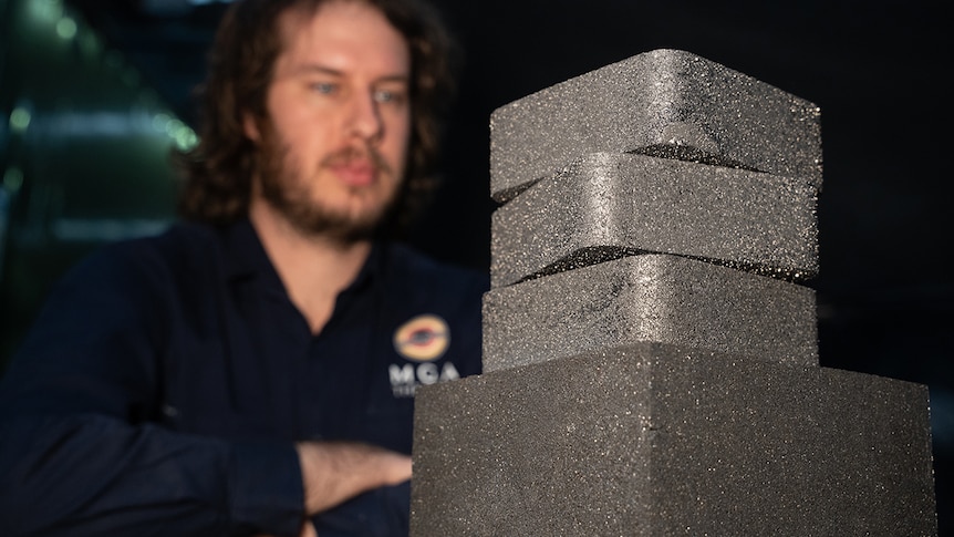 A man looks at a stack of dark shaped blocks.