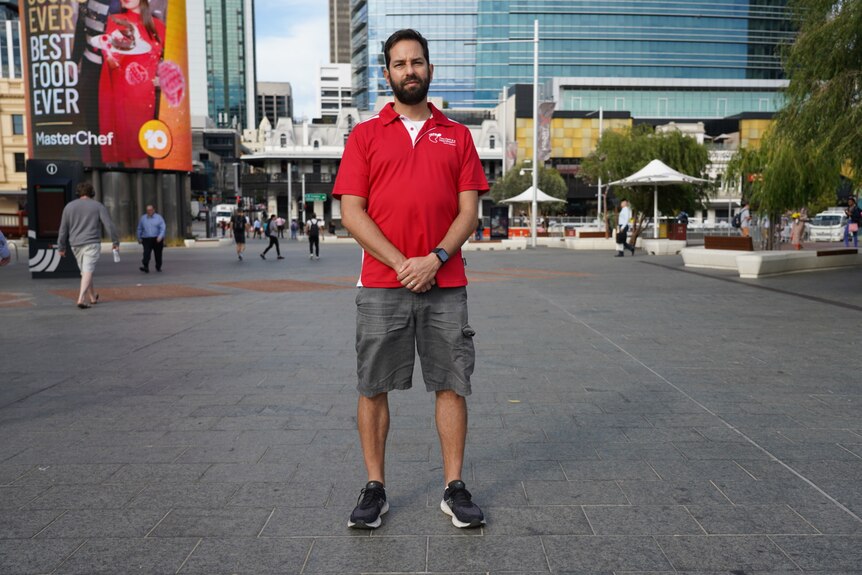 A walking tour operator stands in the middle of the Perth CBD with his arms crossed and a serious expression