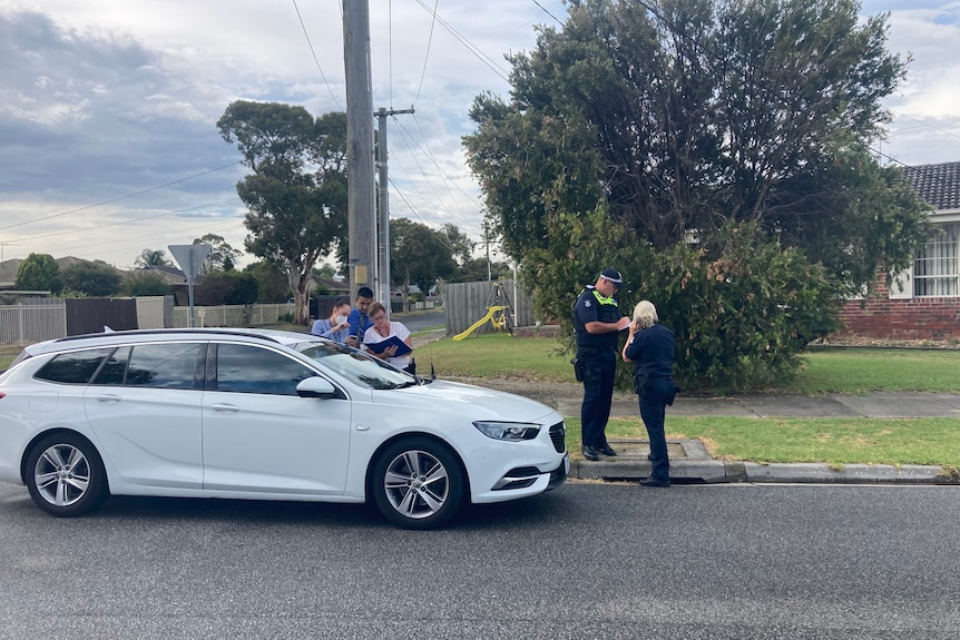 Police interview people in a suburban street in front of a white station wagon