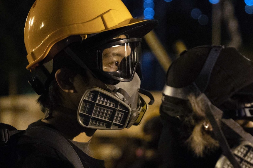 A person wearing a yellow helmet, clear goggles and a gas mask at night.