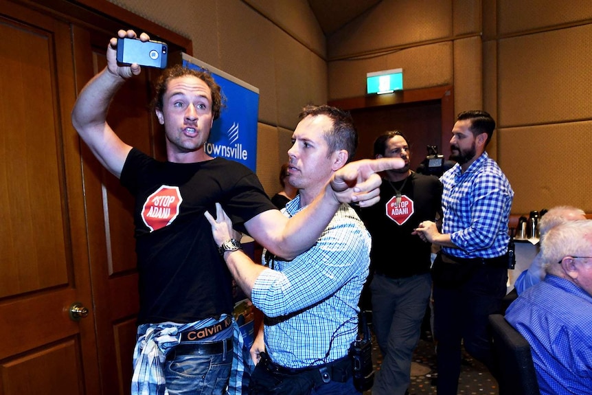 Two men wearing anti-Adani shirts are escorted out of a forum.
