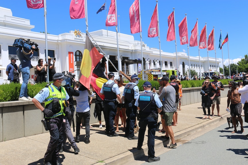 A protester waves a flag outside Old Parliament House, surrounded by police.