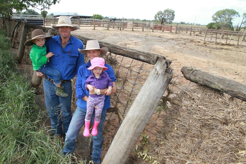 Two adults and two children stand in front of flood-damaged cattle yards.