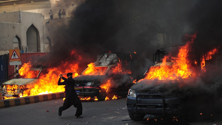 A demonstrator brandishes a stick near burning police vehicles during a protest against an anti-Islam film in Karachi.