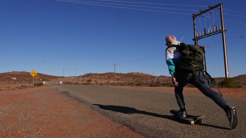 A skateboarder pushing down an outback road.