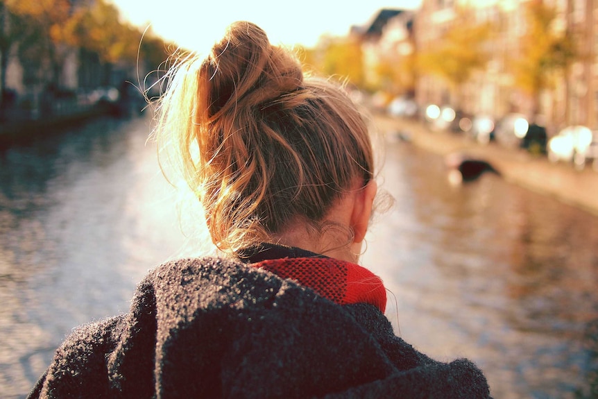 A woman, photographer from behind, looks out on a body of water.