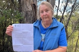 A woman holds up a notice while standing in front of forests.
