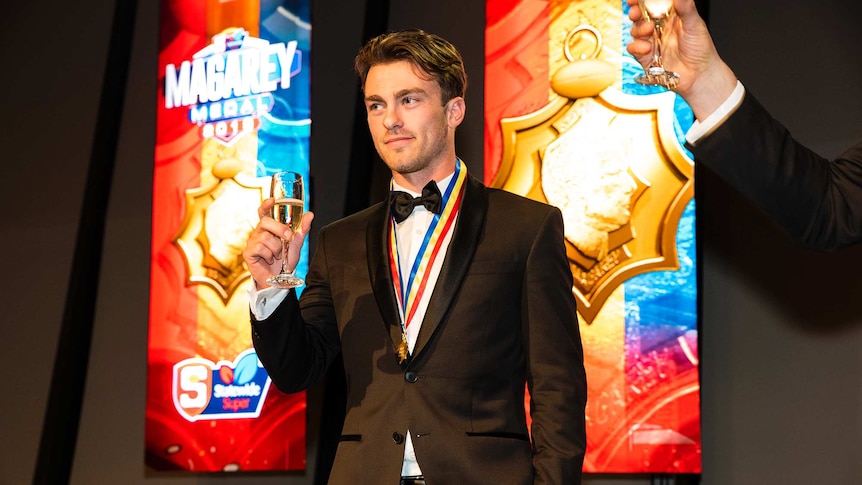 Dashing young man wears tuxedo and colourful medal around his neck as he rasies a glass of champagne