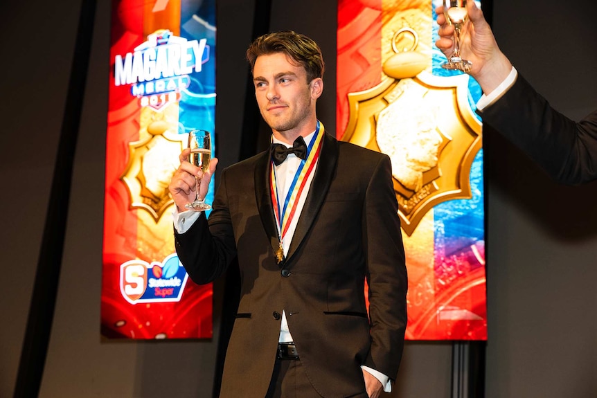 Dashing young man wears tuxedo and colourful medal around his neck as he rasies a glass of champagne