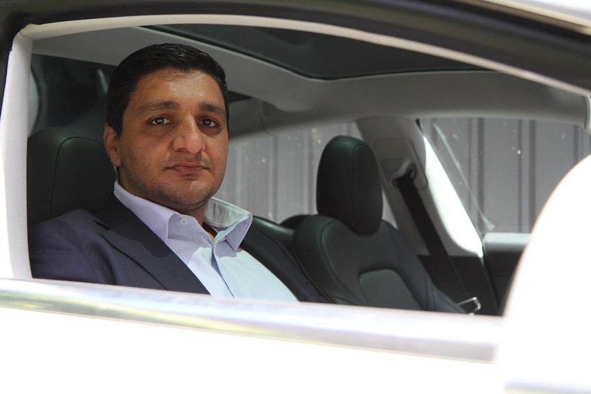 Beyhad Jafari sentado en el asiento del conductor de un coche, mirando por la ventanilla a la cámara.
