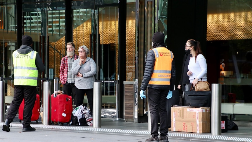 Men and women, some wearing masks, with baggage wait for cabs outside Crown casino.