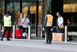 Men and women, some wearing masks, with baggage wait for cabs outside Crown casino.