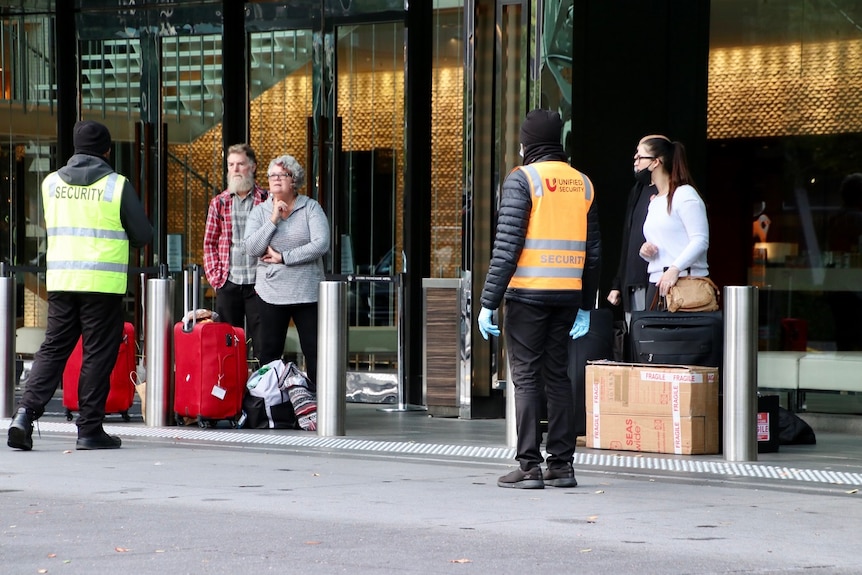 Men and women, some wearing masks, with baggage wait for cabs outside Crown casino.