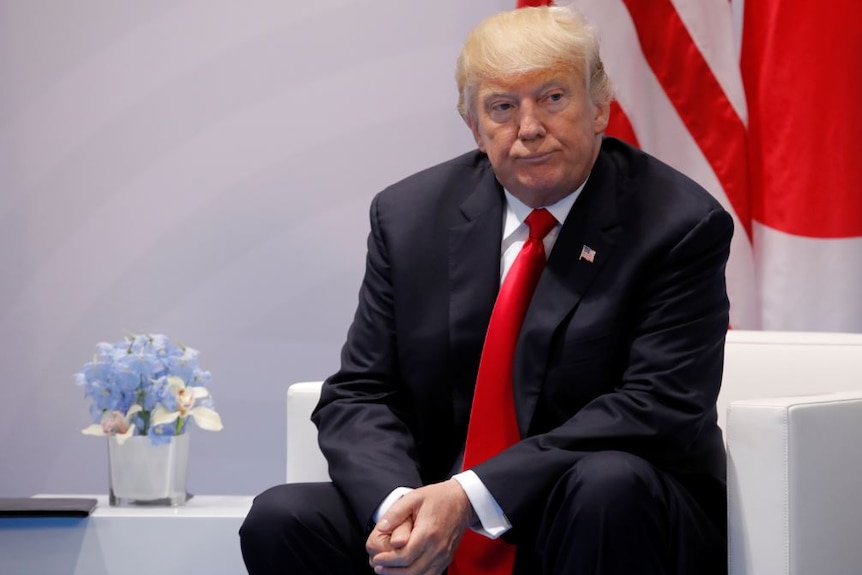 Donald Trump, seated near an American flag, wears a frustrated expression.