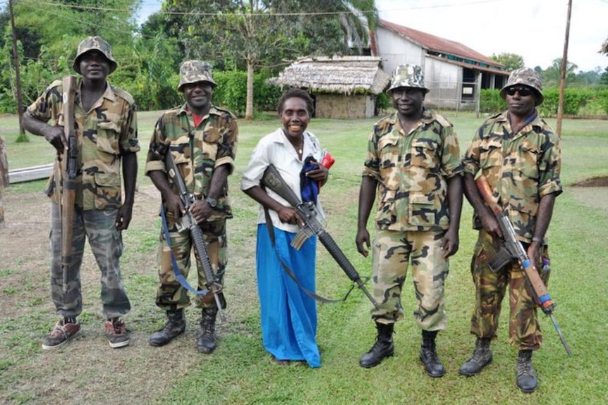 A women stands between a group of soldiers holding a gun.